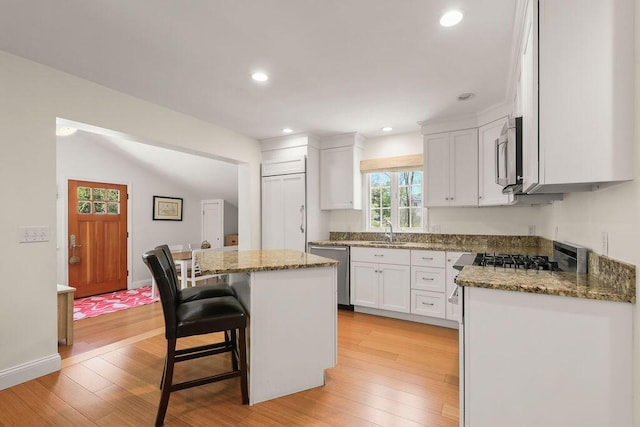 33 Beach Rd, Orleans, MA 02653 - kitchen with appliances with stainless steel finishes, a center island, white cabinets, light wood finished floors, and dark stone counters