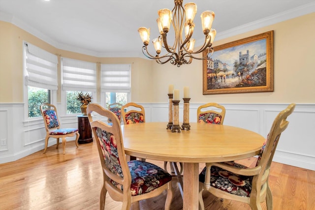 dining area featuring light wood-style floors, a decorative wall, a chandelier, a wainscoted wall, and ornamental molding
