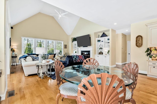 dining space with visible vents, light wood-style floors, ceiling fan, and a glass covered fireplace