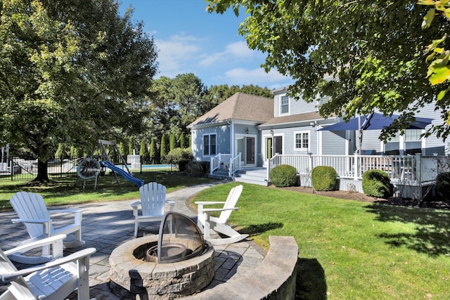 rear view of property with fence, a shingled roof, a patio area, an outdoor fire pit, and a yard