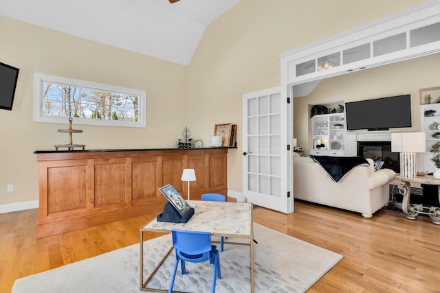 office featuring a glass covered fireplace, baseboards, vaulted ceiling, and light wood-type flooring