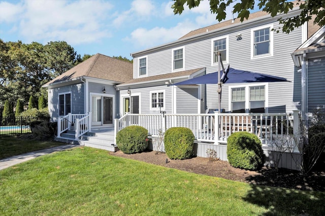rear view of property featuring roof with shingles, a yard, and a deck