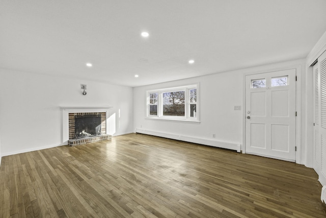 unfurnished living room with a brick fireplace, dark hardwood / wood-style floors, and a baseboard heating unit