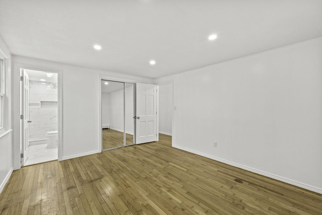 unfurnished bedroom with hardwood / wood-style flooring, ensuite bathroom, and a closet