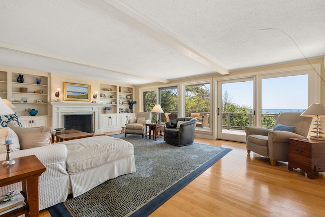 142 Greely Ave, Centerville, MA 02632 - living room with light wood-style floors, a textured ceiling, beamed ceiling, a fireplace, and built in shelves