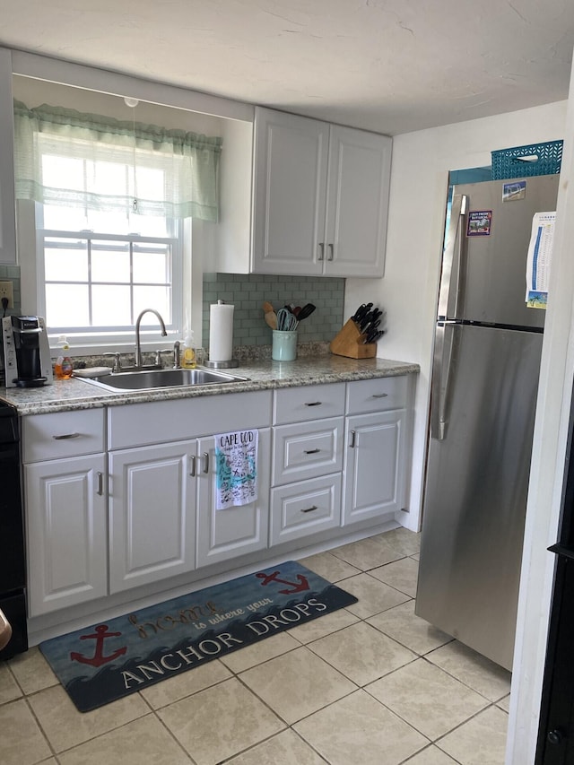 kitchen featuring light tile patterned floors, white cabinets, stainless steel fridge, and sink