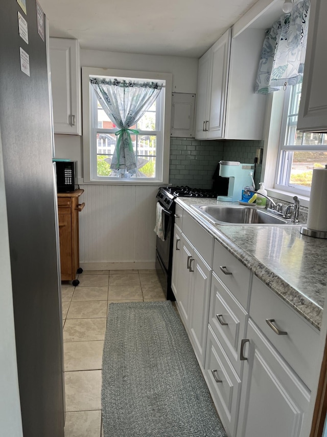 kitchen featuring white cabinetry, black gas range oven, decorative backsplash, sink, and light tile patterned flooring