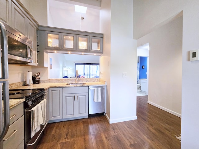 kitchen featuring stainless steel appliances, a sink, gray cabinets, dark wood-type flooring, and a towering ceiling