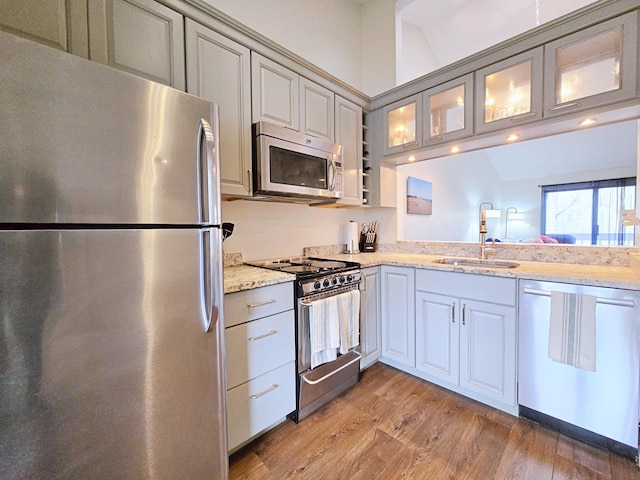 kitchen featuring appliances with stainless steel finishes, a sink, glass insert cabinets, light wood-style flooring, and gray cabinetry