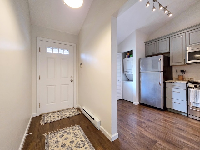 doorway to outside with stacked washer / drying machine, a baseboard radiator, vaulted ceiling, dark wood-style floors, and baseboards