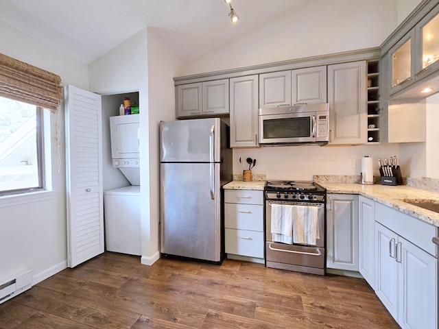 kitchen featuring stainless steel appliances, stacked washer and clothes dryer, lofted ceiling, a baseboard radiator, and gray cabinets