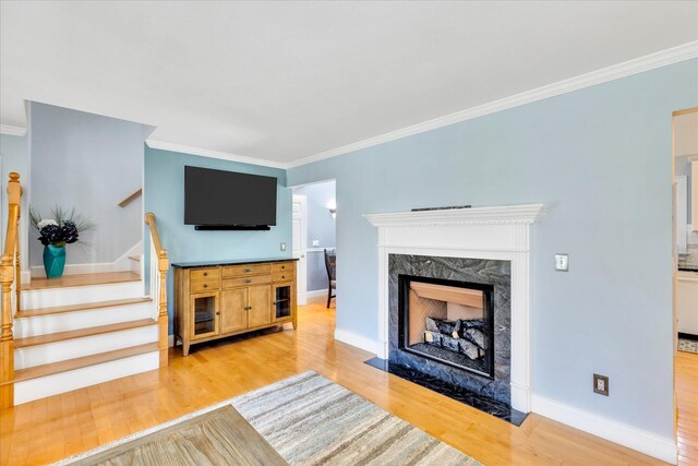 unfurnished living room featuring ornamental molding, light wood-style flooring, stairs, and a fireplace