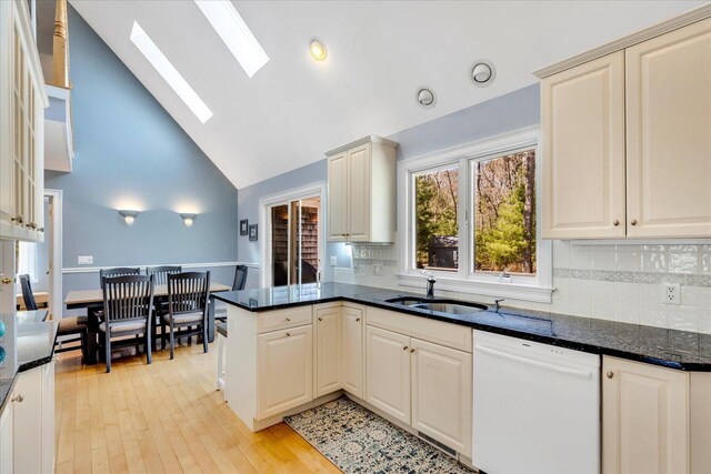 kitchen with a sink, dishwasher, dark stone countertops, tasteful backsplash, and a skylight