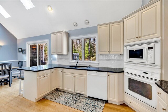 kitchen with a peninsula, white appliances, light wood-style floors, lofted ceiling with skylight, and backsplash