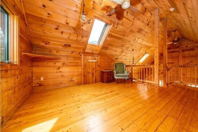 bonus room featuring vaulted ceiling with skylight, wood walls, and hardwood / wood-style flooring