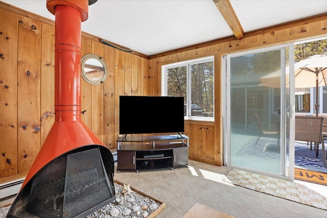 living area featuring beamed ceiling, wood walls, carpet flooring, and a wood stove
