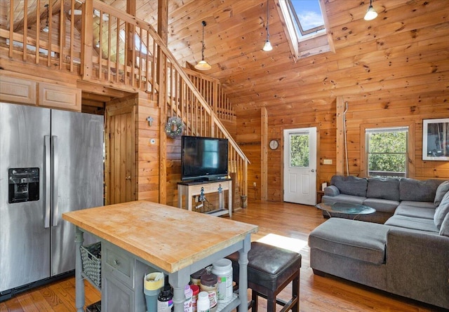 living area with a skylight, light wood finished floors, wood walls, high vaulted ceiling, and stairs