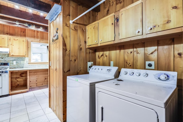 clothes washing area featuring cabinets, washing machine and clothes dryer, and wooden walls