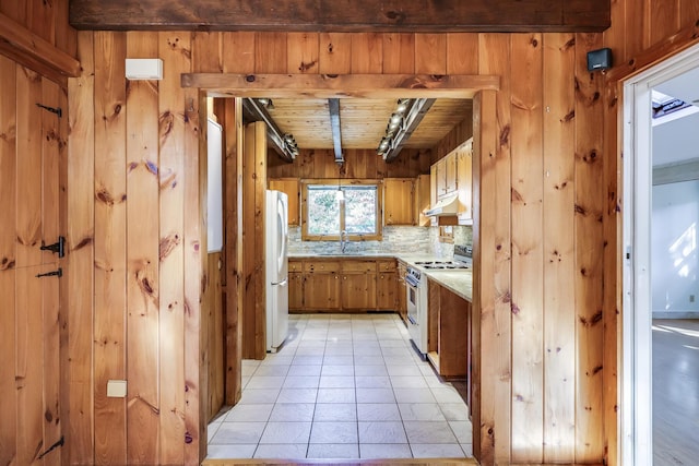 kitchen featuring sink, stainless steel range, wood walls, and white refrigerator