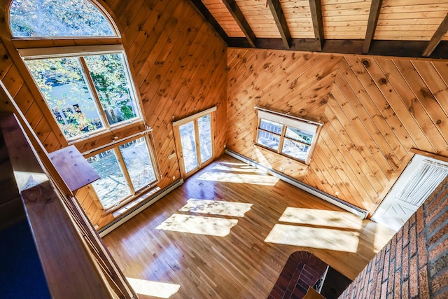 unfurnished living room featuring wood walls, a skylight, high vaulted ceiling, beamed ceiling, and a baseboard heating unit