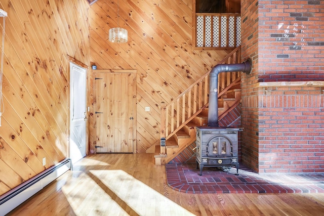 unfurnished living room with wood walls, hardwood / wood-style floors, a wood stove, and a baseboard heating unit