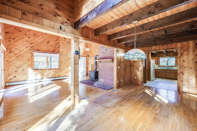 interior space featuring beamed ceiling, a baseboard radiator, a wood stove, wood ceiling, and light wood-type flooring