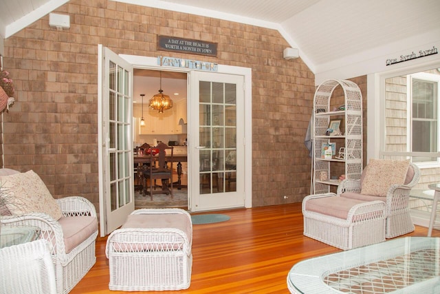 sitting room featuring lofted ceiling, brick wall, an inviting chandelier, and wood finished floors