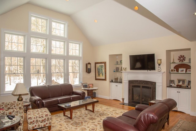 living room featuring high vaulted ceiling, light wood finished floors, a premium fireplace, and baseboards