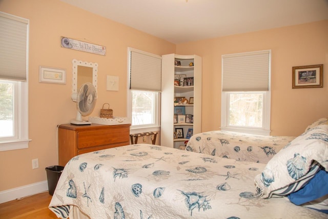 bedroom featuring multiple windows, baseboards, and wood finished floors