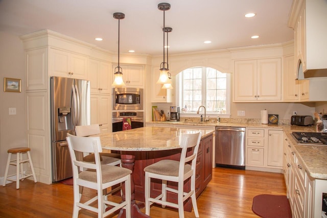 kitchen with light stone counters, appliances with stainless steel finishes, a sink, a kitchen island, and wood finished floors
