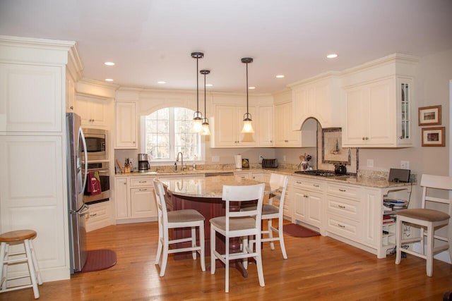 kitchen with a breakfast bar area, a sink, appliances with stainless steel finishes, a center island, and light wood finished floors