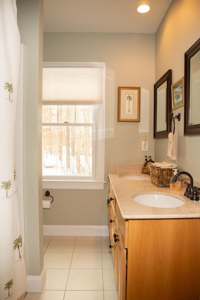 full bathroom with double vanity, tile patterned flooring, a sink, and baseboards