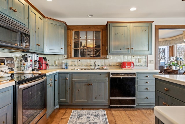 kitchen with black appliances, backsplash, a sink, light countertops, and recessed lighting