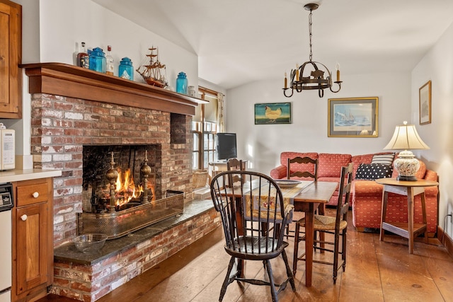 dining room featuring light wood-style flooring, a chandelier, lofted ceiling, and a fireplace