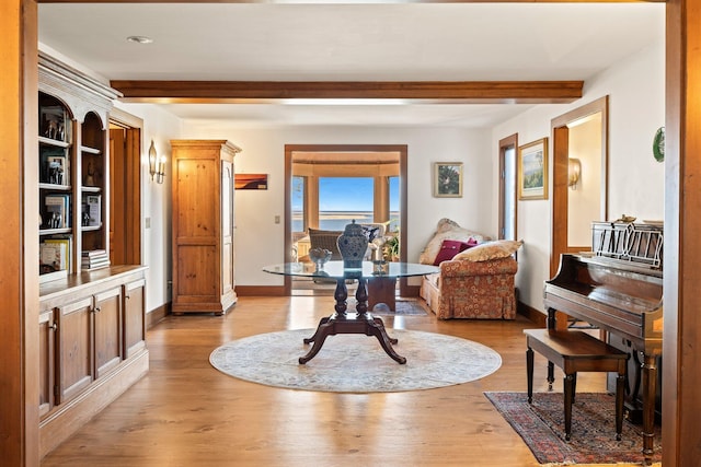 sitting room featuring beam ceiling, baseboards, and light wood finished floors