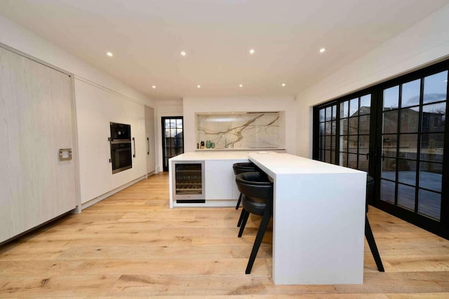 kitchen with kitchen peninsula, light hardwood / wood-style floors, a breakfast bar, and beverage cooler