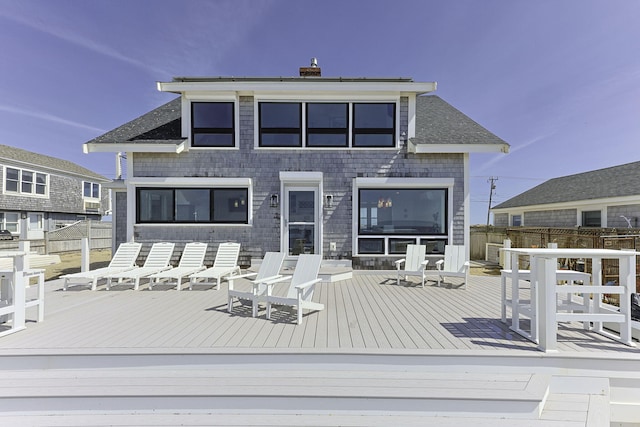 back of property with a wooden deck, a chimney, and fence