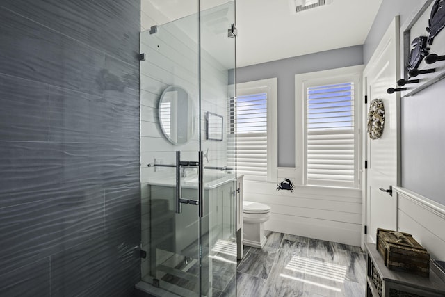 bathroom featuring wainscoting, toilet, visible vents, and a shower stall