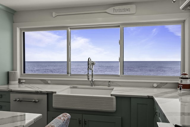 kitchen with a sink, a water view, plenty of natural light, and light stone counters