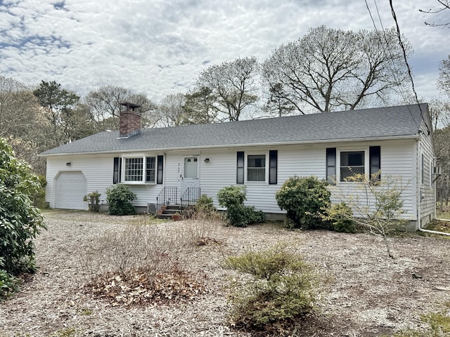 ranch-style home with a garage, a chimney, and roof with shingles