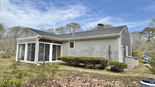 back of property with a sunroom, a chimney, roof with shingles, and central air condition unit