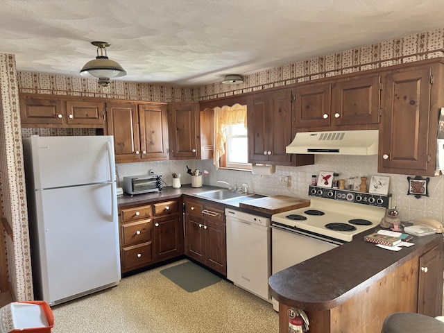 kitchen with white appliances, exhaust hood, a sink, dark countertops, and wallpapered walls