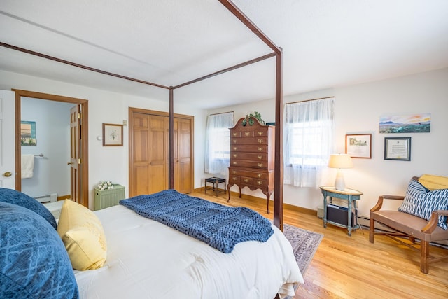 bedroom with a closet, baseboard heating, and light wood-type flooring
