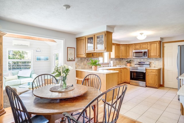 kitchen featuring backsplash, a wall mounted AC, light countertops, glass insert cabinets, and stainless steel appliances