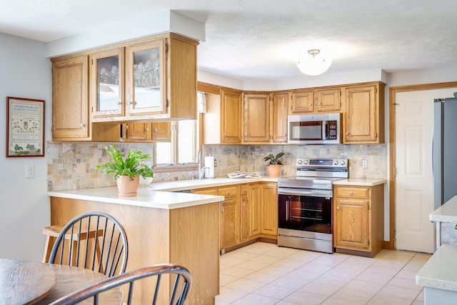 kitchen featuring appliances with stainless steel finishes, light countertops, a peninsula, backsplash, and glass insert cabinets