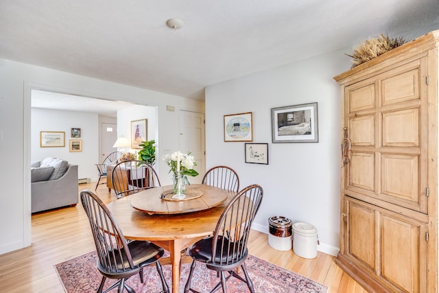 dining space with baseboards, a baseboard heating unit, and light wood-style flooring