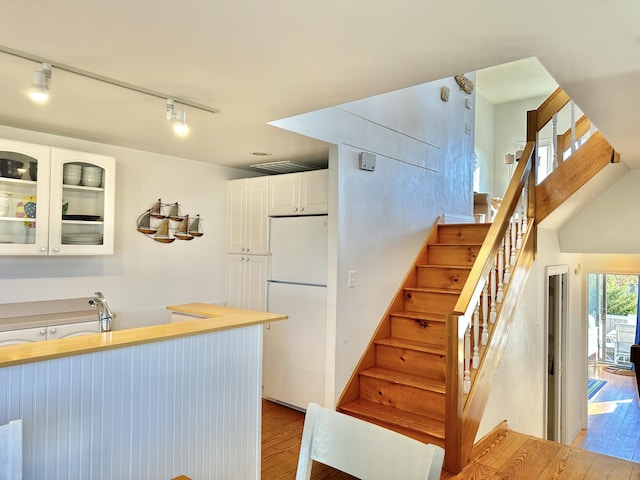 kitchen with white cabinets, light wood-type flooring, track lighting, and white fridge