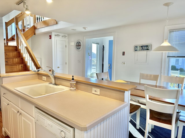 kitchen featuring hanging light fixtures, white dishwasher, sink, white cabinets, and an island with sink