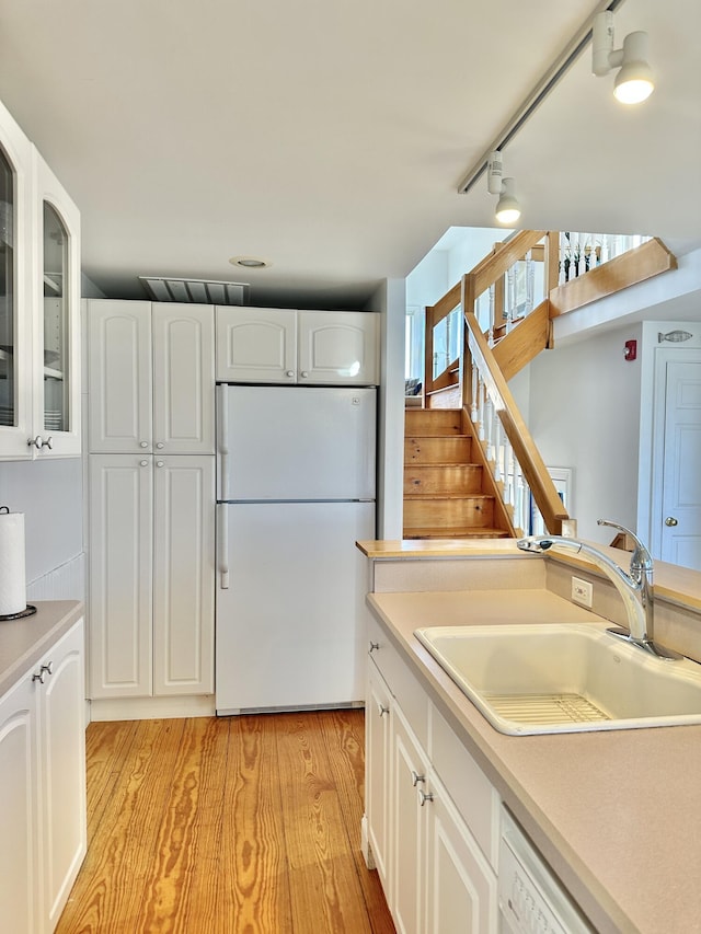 kitchen with white appliances, white cabinetry, sink, rail lighting, and light hardwood / wood-style flooring