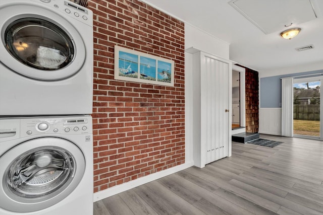 washroom with stacked washing maching and dryer, brick wall, and light hardwood / wood-style floors